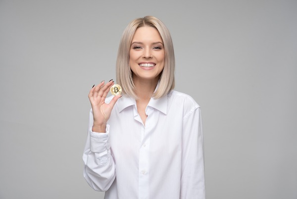 Smiling woman in a white shirt holding a gold Bitcoin coin