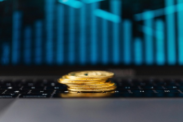Stack of gold cryptocurrency coins on a laptop keyboard with a blue price chart glowing on the screen behind them