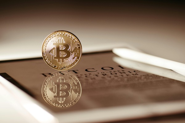 Gold Bitcoin coin balanced upright on a printed Bitcoin whitepaper document