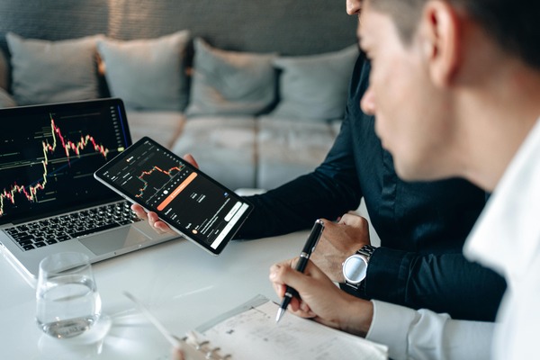 Two people reviewing a cryptocurrency candlestick chart on a laptop and tablet