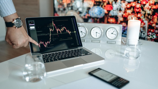 Laptop showing a cryptocurrency price chart on a desk with clocks, a candle, and a phone