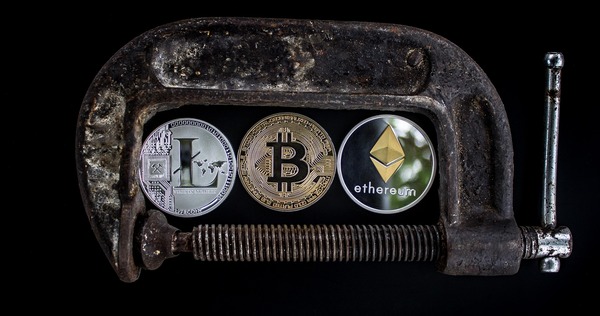 Litecoin, Bitcoin, and Ethereum coins gripped inside a rusty metal clamp